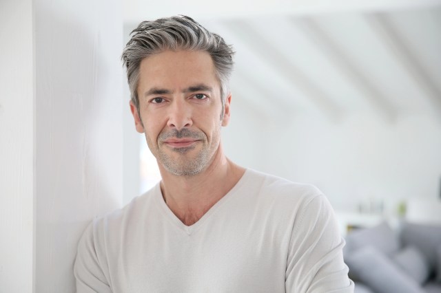 Portrait of a man in his 50s with gray hair standing indoors in a bright, modern home